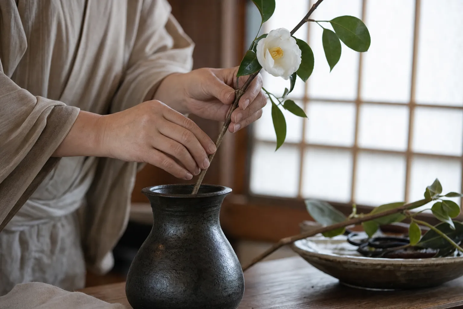 障子越しの光の中、花器に椿の枝を挿す手元