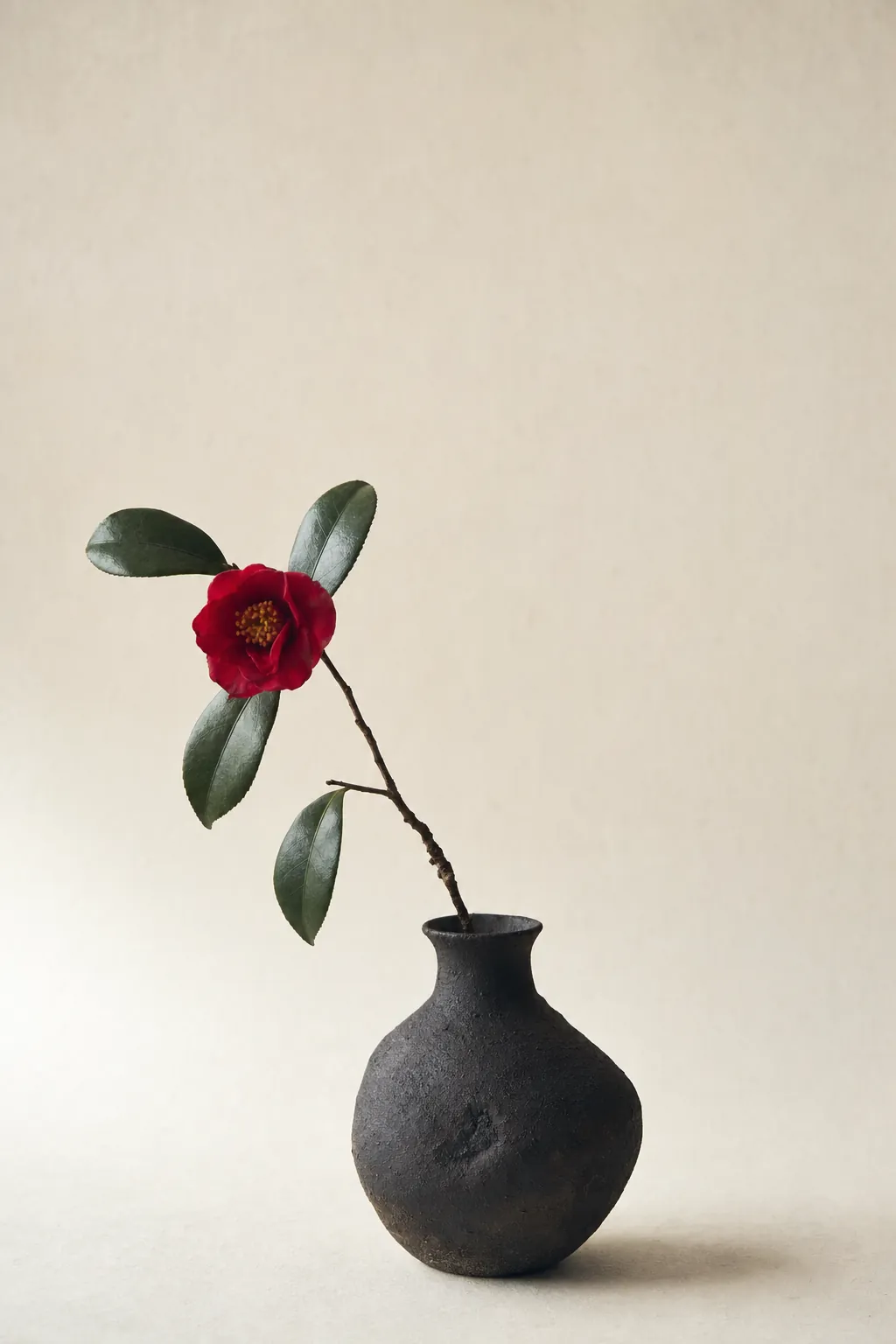 黒い備前の花器に活けられた一輪の深紅の椿。生成りの和紙を背景にした余白の多い構図